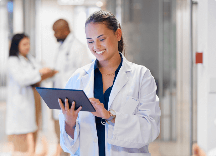 smiling female doctor charting on her tablet with medical workers in the background